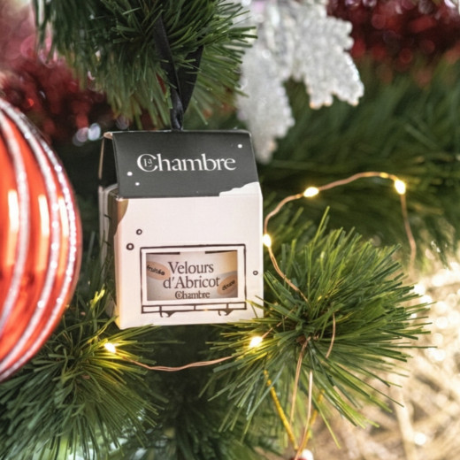 Boule de Noël Velours d'Abricot suspendue dans un sapin illuminé, entre une boule rouge et un flocon