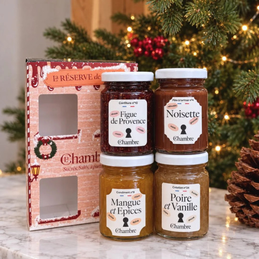 Les quatre pots de 100 g du coffret de Noël devant un sapin illuminé : figue, noisette, mangue-épices, poire-vanille