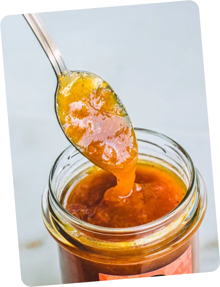 A spoonful of peach apricot jam dripping into a gourmet golden-looking jam jar