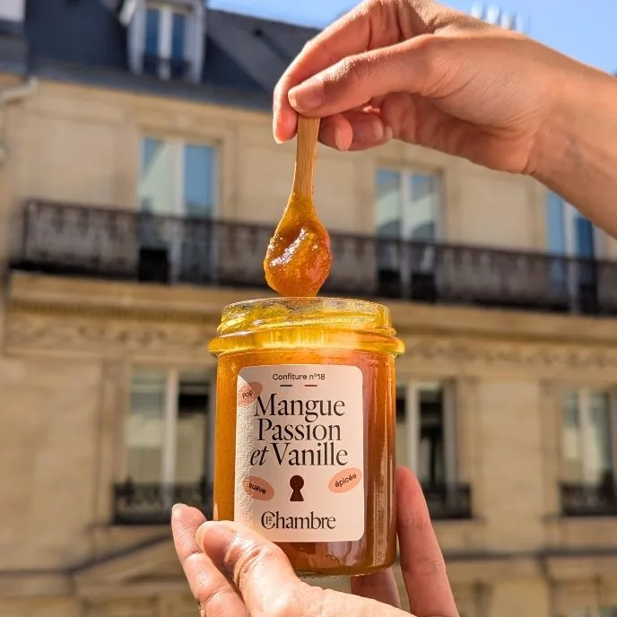 Jar of Mango Passion and Vanilla jam held up in front of a Parisian building